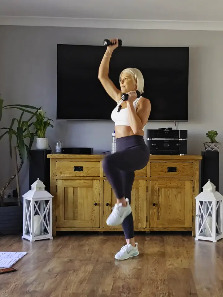 Anna lifting a knee with light dumbbells