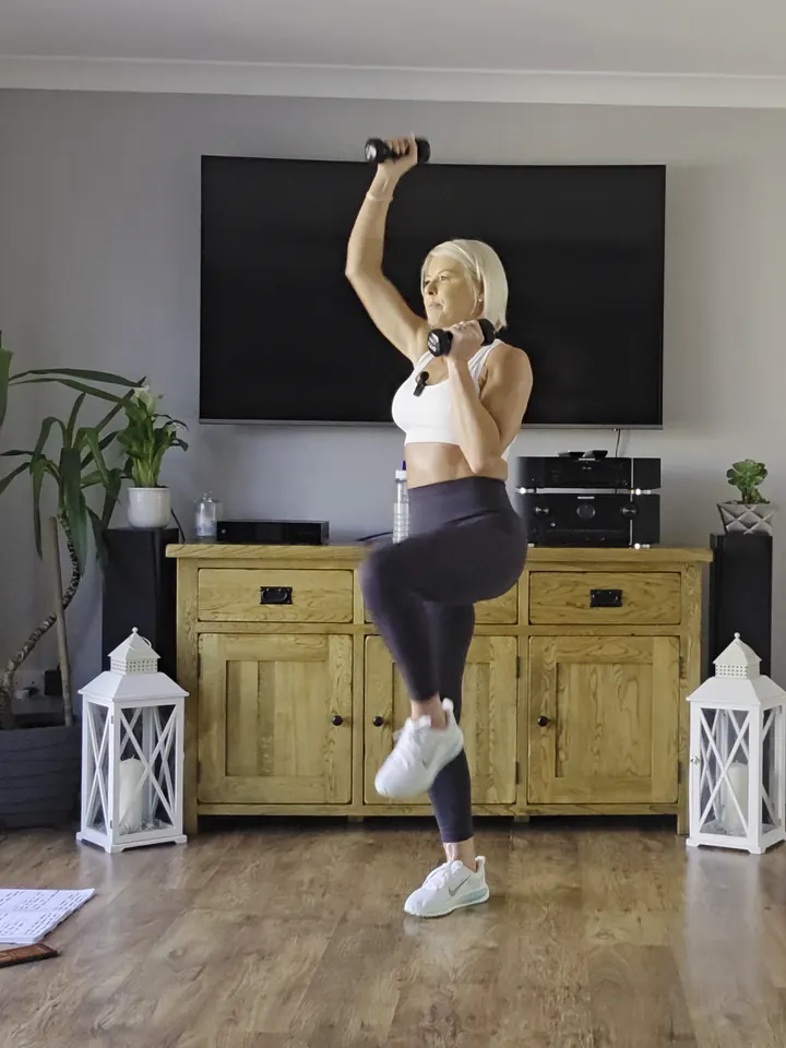 Anna lifting a knee with light dumbbells